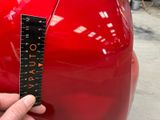 someone is measuring the height of a red car with a ruler