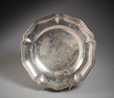 un plat ancien en argent posé sur un socle, sur une surface grise