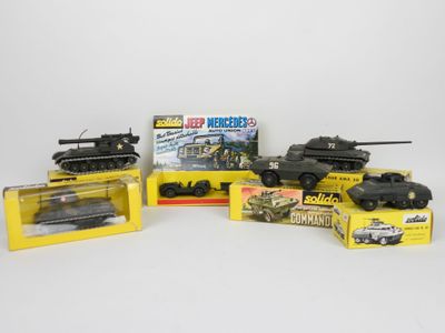 trois chars miniatures et une petite voiture dans une boîte posée sur une surface blanche