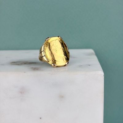 La bague en or repose sur un bloc de marbre blanc.