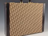 Une vieille valise munie d'une poignée est posée sur une surface blanche.