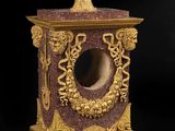 une horloge en marbre doré et rouge, surmontée d'un bol
