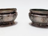 two silver pots sitting next to each other on a white surface