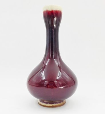 un vase rouge posé sur une surface blanche