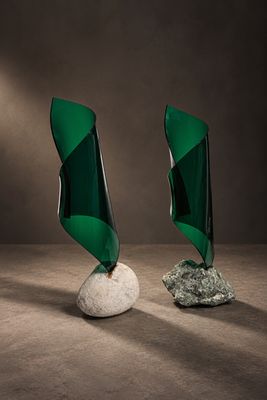 une paire de sculptures en verre vert posées sur un rocher blanc