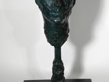 sculpture en bronze représentant une tête, posée sur un socle noir, sur fond blanc