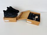 Deux paires de baskets noires se trouvent dans une boîte posée sur une surface blanche