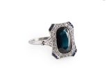un gros plan d'une bague posée sur une surface blanche, ornée d'une pierre bleue