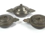 trois objets d'art liturgique anciens posés sur une surface blanche, sur fond blanc