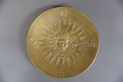 une médaille d'or sur laquelle est représenté un soleil, posée sur un fond blanc