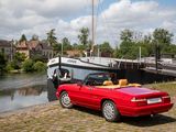 a red convertible car parked next to a boat on the water