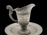 une assiette en argent ancien posée sur une soucoupe, sur fond noir