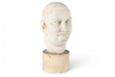 tête d'homme en plâtre posée sur un socle en bois, devant un fond blanc