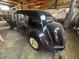an old black car parked in a garage with a man standing next to it