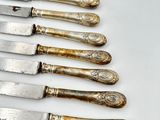 six silverplated knives are lined up in a row on a white surface