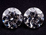 a pair of round cut diamonds on a black surface