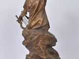 bronze statue of a woman playing a harp on a rock