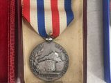a silver medal with a red, white, and blue ribbon in a box