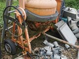 a cement mixer sitting on the ground next to a pile of pipes