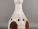 a white vase with brown spots on it on a gray surface