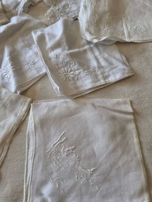four white napkins with embroidered flowers on them on a bed