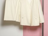 two pieces of white clothing hanging on a rack in front of a pink and white wall