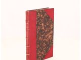 an old book with a red cover sitting on top of a white surface