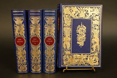 trois livres bleus ornés de motifs dorés, posés sur une table