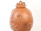 un vase marron muni d'un couvercle, posé sur une surface blanche