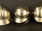 three silver fire helmets sitting on top of a black table