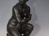 bronze statue of a female nude sitting on a rock with her arms crossed