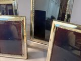 three silver picture frames are sitting on a table with a white table cloth