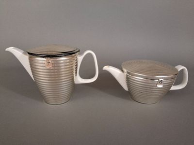 une paire de cafetières argentées et blanches avec couvercles, posées sur un plan de travail gris
