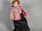 une image représentant une poupée à l'effigie d'une femme vêtue d'un manteau rose et d'une robe noire