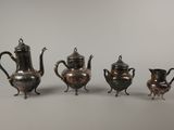 trois théières en argent et une cafetière sur une table