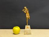 gold figurine of a woman holding a flute and an apple on a wooden table