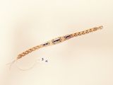 a gold bracelet with blue stones on it on a white surface