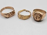 three gold rings with initials on them sitting on a white surface