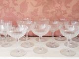 several empty wine glasses lined up on a table with a wallpapered wall behind them