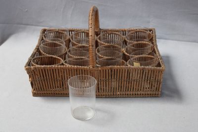des bouteilles dans un panier en osier, avec un verre posé sur une table