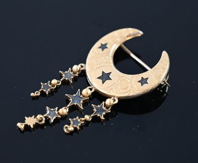 un gros plan d'une broche représentant un croissant de lune et des étoiles sur un fond noir