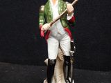 figurine of a man in a green jacket and white pants holding a cane
