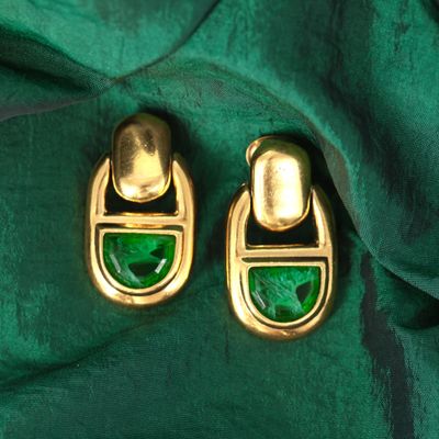 une paire de boucles d'oreilles vertes et dorées posées sur un tissu vert