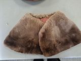 a brown fur cape on a white table with a clock on the wall in the background