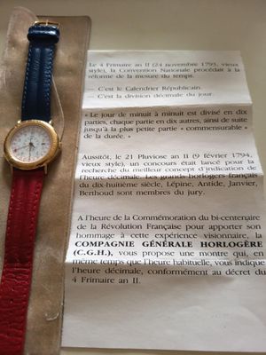 une montre posée sur une feuille de papier, à côté d'une autre feuille de papier à laquelle est attachée une feuille de papier