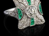 un gros plan d'une bague sertie d'un diamant et d'une émeraude sur une surface noire