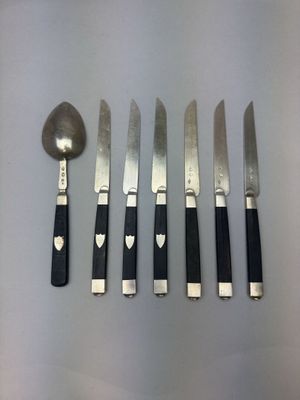 six couteaux et une cuillère sont alignés sur une table