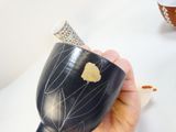 une personne tenant un vase noir orné d'une feuille d'or