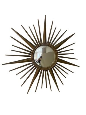 un gros plan d'un miroir accroché au mur, orné d'un motif en rayons de soleil