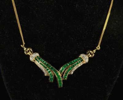 a gold necklace with green and white stones on a black mannequin